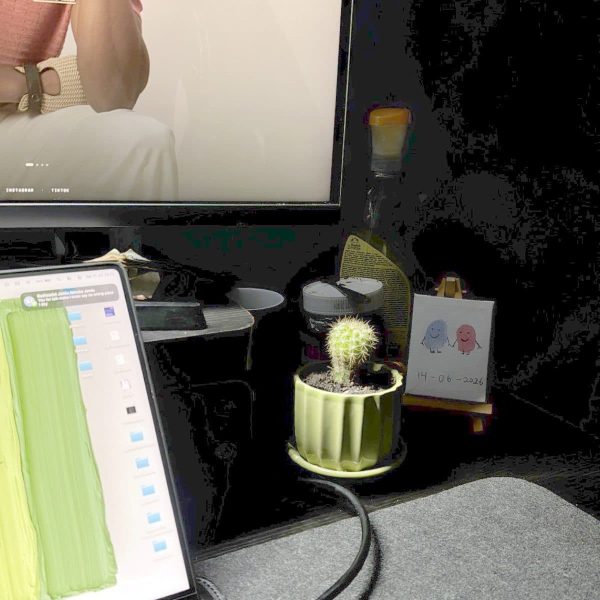A small cactus in a green pot next to a framed fingerprint painting.